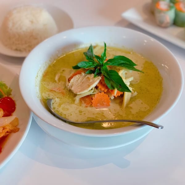 A bowl of green curry with chicken, carrots, and basil, served with a side of rice.