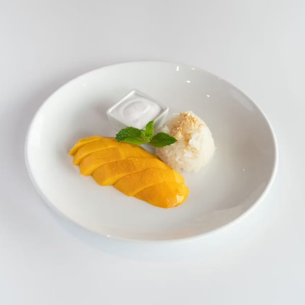 Mango sticky rice dessert with coconut milk and mint on a white plate.