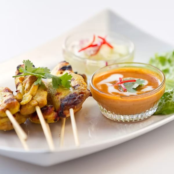 Grilled chicken satay skewers with peanut sauce and cucumber relish, garnished with cilantro.