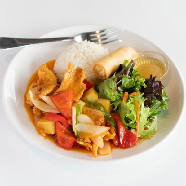 Sweet and sour chicken with rice, egg roll, and salad on a white plate with a fork.