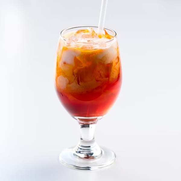A vibrant Thai iced tea with red and orange layers, topped with cream and a white straw.