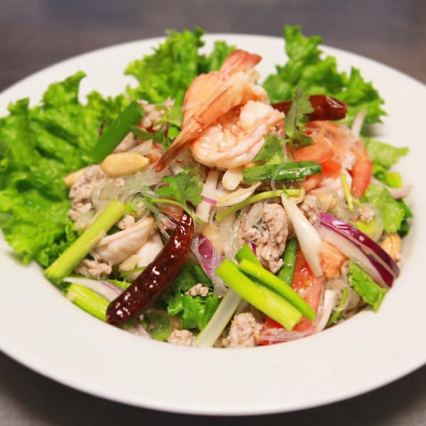 Thai glass noodle salad with shrimp, minced pork, vegetables, and dried chili on a white plate.