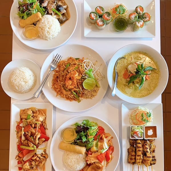 An overhead view of a table laden with various Thai dishes, including curries, noodles, and spring rolls.