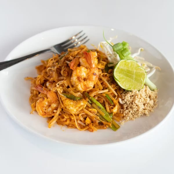 A plate of Pad Thai with shrimp, lime, bean sprouts, and crushed peanuts, with a fork.