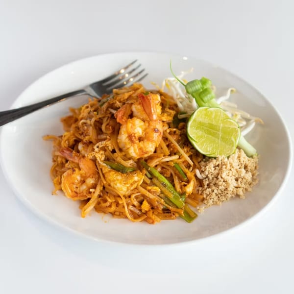 A plate of shrimp Pad Thai with lime, bean sprouts, and crushed peanuts on a white plate.