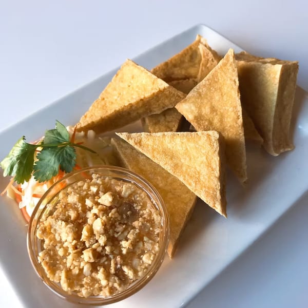 Golden fried tofu triangles with a side of peanut sauce and a garnish of cilantro.