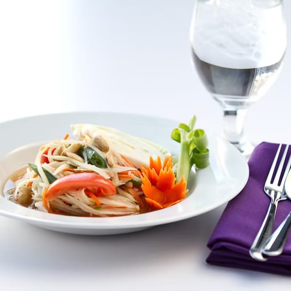 Som Tum (papaya salad) with peanuts, tomatoes, and a carrot garnish, next to a water glass.