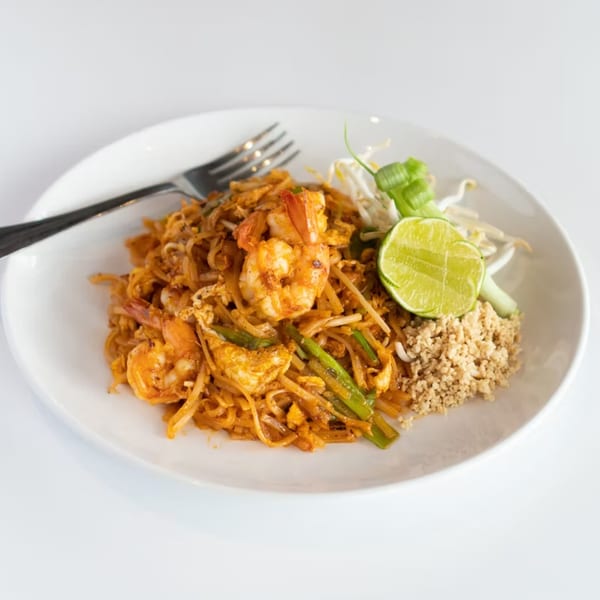 A plate of shrimp Pad Thai with noodles, green onions, bean sprouts, lime, and crushed peanuts.