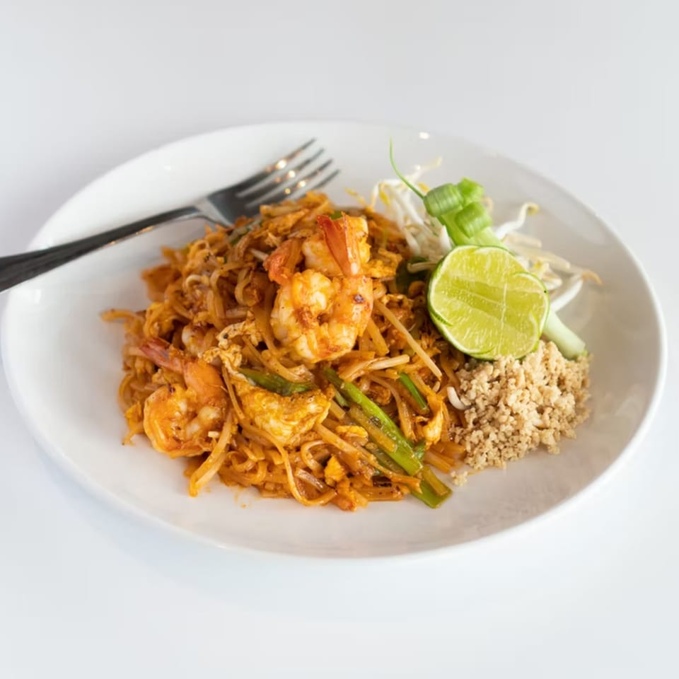 A plate of shrimp Pad Thai with noodles, green onions, bean sprouts, lime, and crushed peanuts.