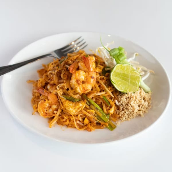 A plate of Pad Thai with shrimp, lime, bean sprouts, and crushed peanuts, with a fork.