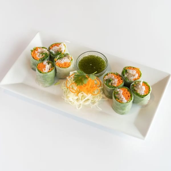 Eight fresh Thai spring rolls with shredded carrots, lettuce, and white filling, served with green dipping sauce.