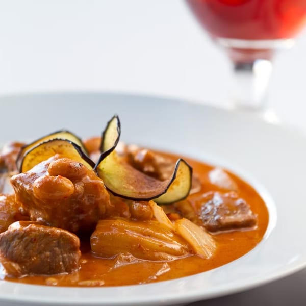 Close-up of a Thai curry dish with meat, vegetables, and a red drink in the background.